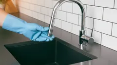 Hand mit blauen Handschuhen reinigt Wasserhahn in moderner Küche mit Spüle