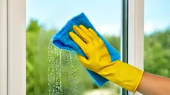 Fensterreinigung mit gelbem Handschuh und blauem Tuch bei Tageslicht