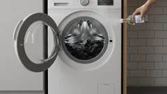 Frontlader-Waschmaschine offen, Hand gießt Flüssigkeit hinein, Wäsche sichtbar