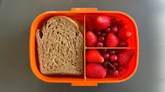 Brot und frische Erdbeeren in orangener Lunchbox, gesunde Pausenmahlzeit für Kinder.